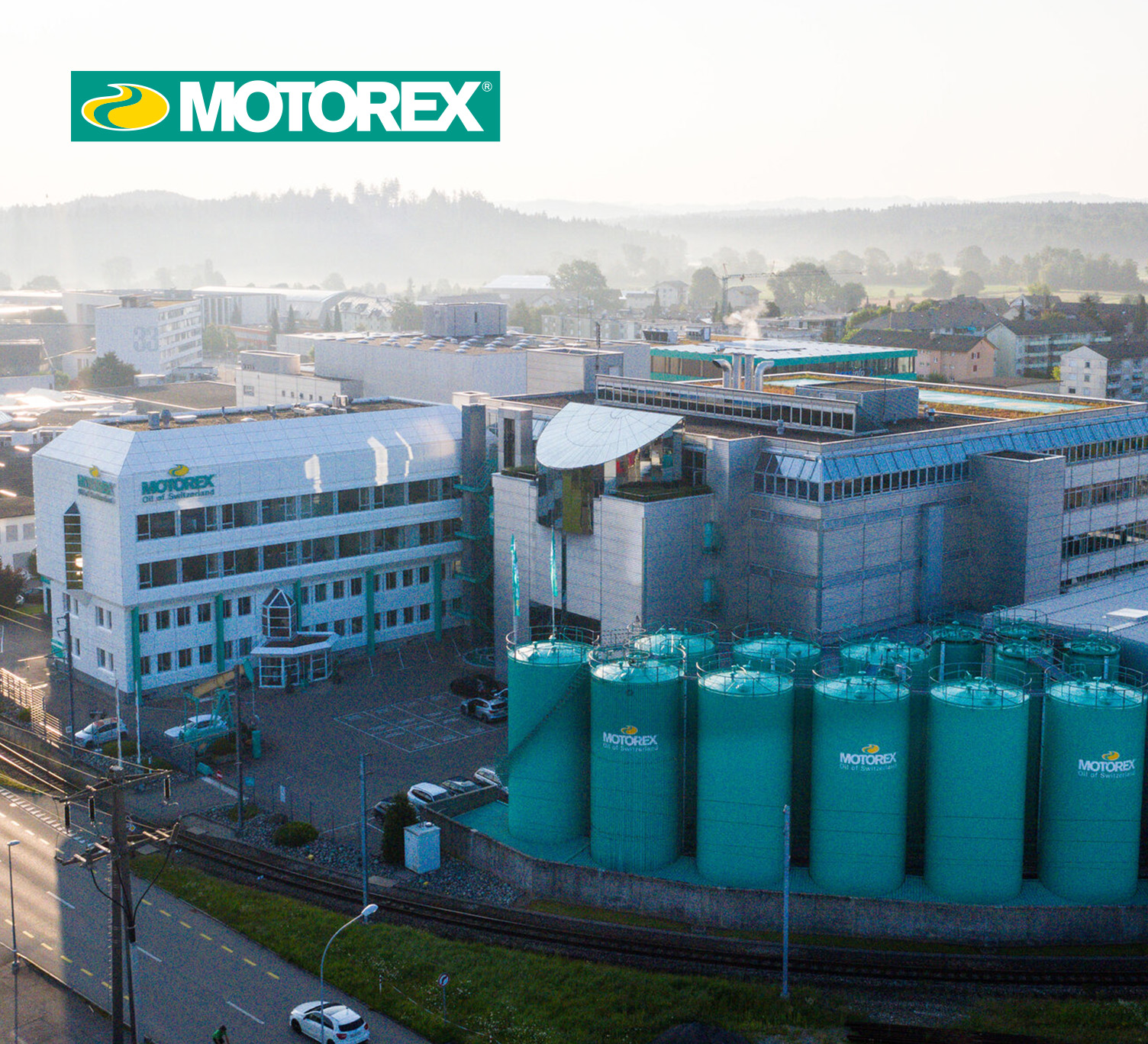Luftaufnahme des MOTOREX-Firmengeländes mit Verwaltungsgebäuden und auffälligen grünen Tanks im Vordergrund, im Hintergrund eine ländlich-industrielle Umgebung.
