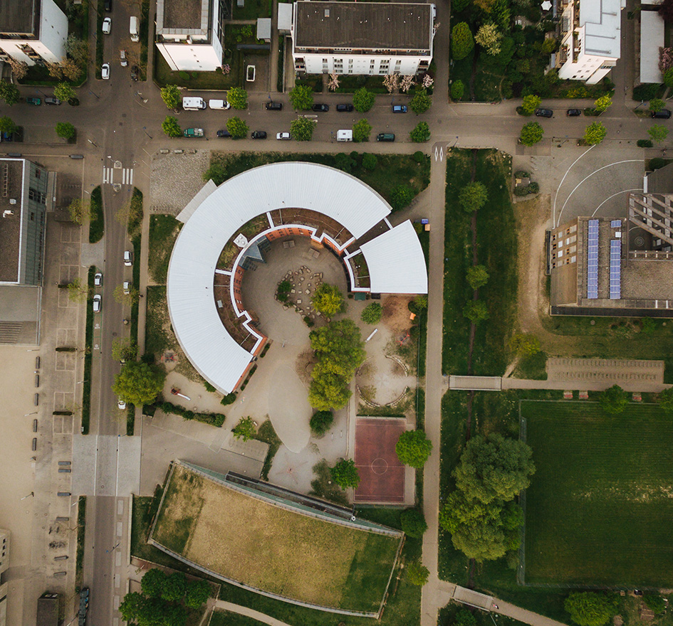 Drohnenaufnahme eines Büro- oder Schulcampus mit markantem, halbkreisförmigem Gebäude, das eine stabile Infrastruktur symbolisiert – passend zum Thema IT-Verfügbarkeit und Ausfallsicherheit.