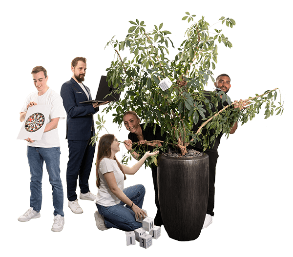 Fünf Personen interagieren spielerisch mit einer großen Zimmerpflanze – mit Laptop, Zielscheibe, Würfeln und Etiketten – Symbol für kreatives Teamwork und Wachstum.