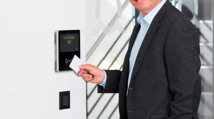 Mann im Anzug lächelt in die Kamera, während er eine Zugangskarte an ein elektronisches Zutrittskontrollsystem hält.