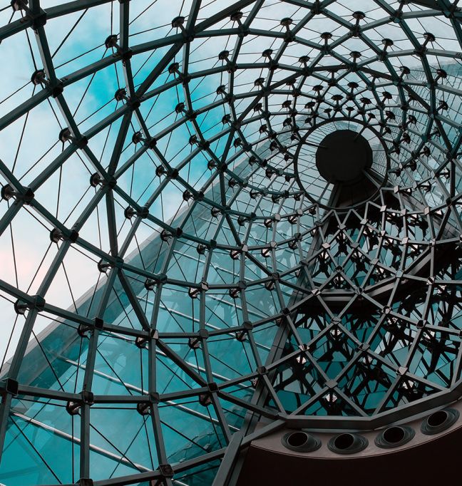 Blick durch eine moderne Glaskuppel mit spiralförmiger Stahlstruktur – symbolisiert komplexe IT-Architekturen und Vernetzung.