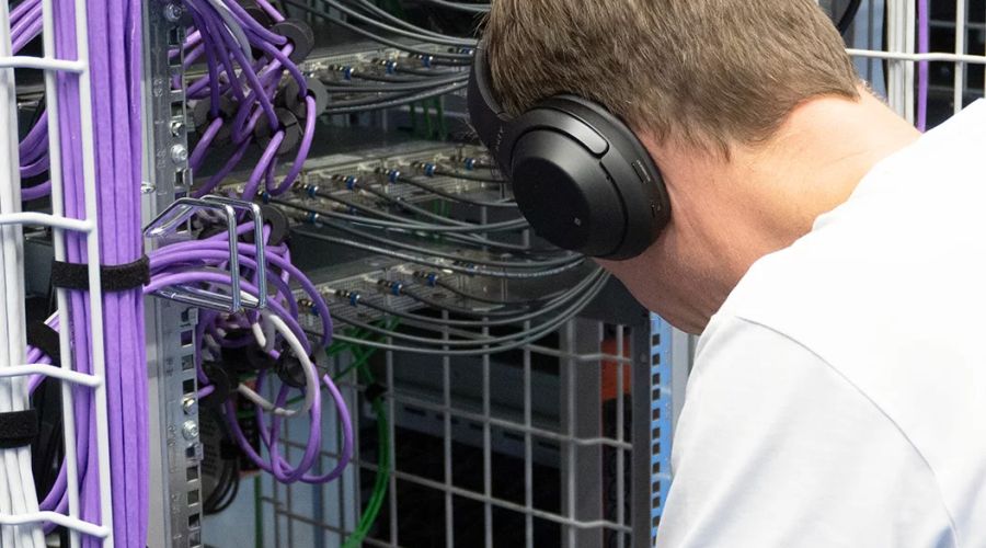 Techniker der WWZ AG arbeitet konzentriert mit Kopfhörern an einem Serverrack voller Netzwerkkabel in einem Rechenzentrum.